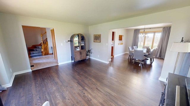 unfurnished dining area featuring stairs, a notable chandelier, baseboards, and dark wood finished floors