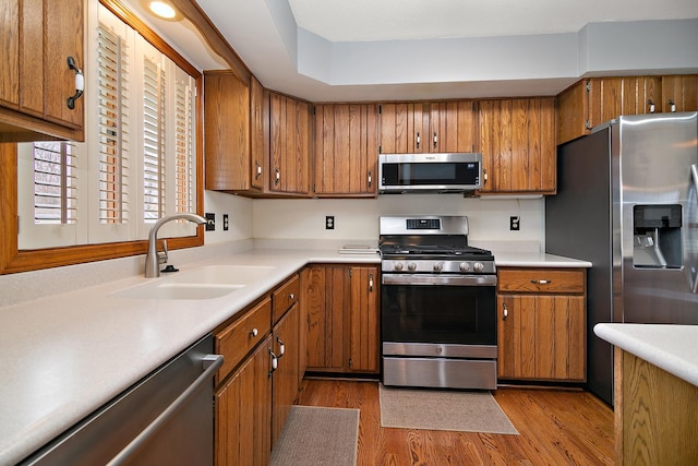 kitchen with light countertops, a sink, wood finished floors, appliances with stainless steel finishes, and brown cabinetry