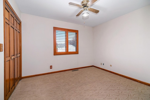 spare room featuring light colored carpet, visible vents, baseboards, and a ceiling fan