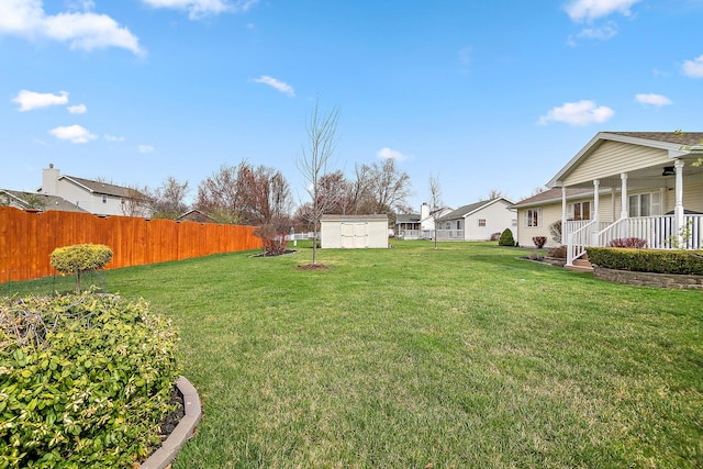 view of yard with an outdoor structure, a fenced backyard, a porch, and a shed