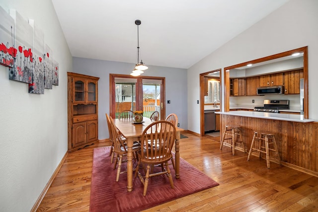 dining area with baseboards, light wood-style flooring, and vaulted ceiling