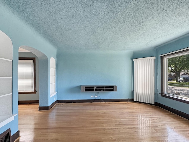 608 W 107th St, Chicago, IL 60628 - unfurnished living room featuring a textured ceiling, wood finished floors, arched walkways, and baseboards