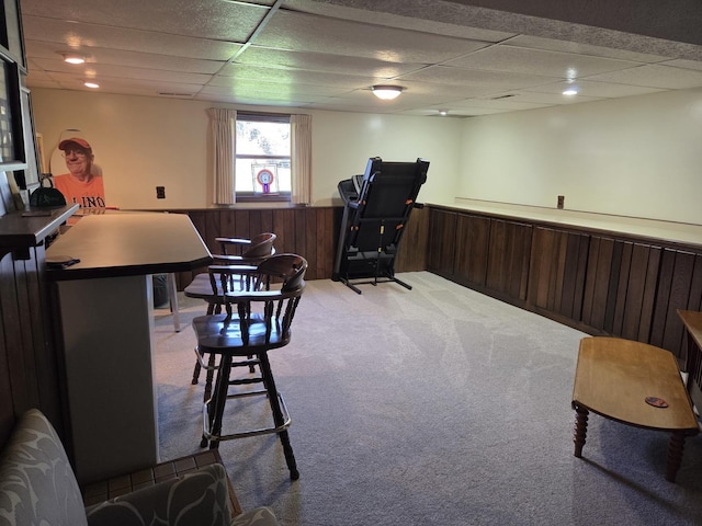 interior space featuring wainscoting, light colored carpet, wooden walls, and a drop ceiling