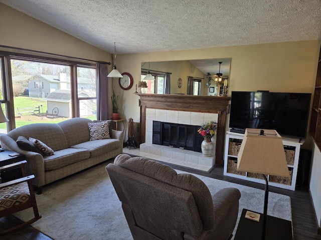 living room with a tiled fireplace, a ceiling fan, a textured ceiling, wood finished floors, and vaulted ceiling