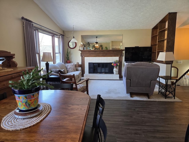 dining space featuring a textured ceiling, wood finished floors, a tiled fireplace, and vaulted ceiling
