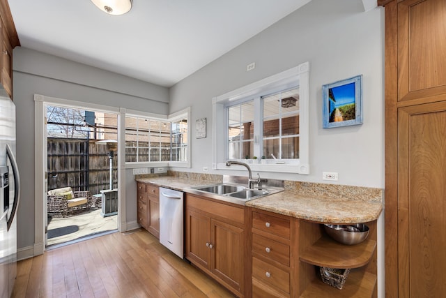 kitchen with light countertops, a sink, dishwasher, brown cabinets, and light wood-style floors