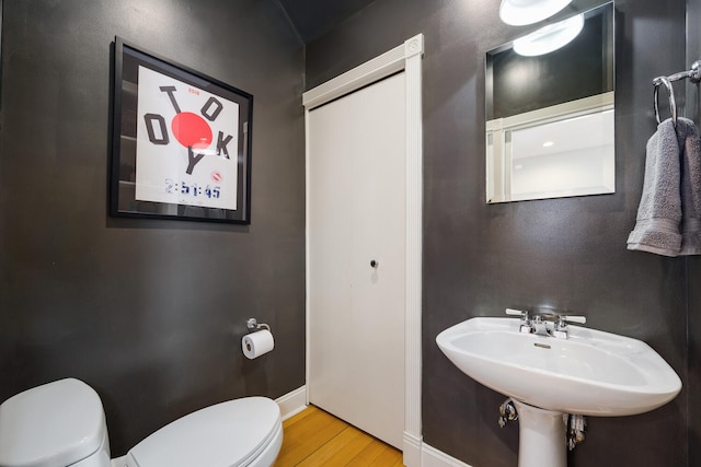 half bathroom featuring baseboards, wood finished floors, toilet, and a sink