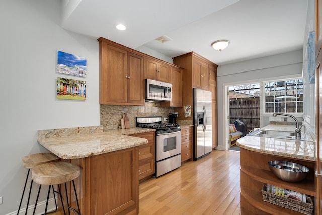 kitchen with a kitchen breakfast bar, tasteful backsplash, appliances with stainless steel finishes, a sink, and brown cabinetry