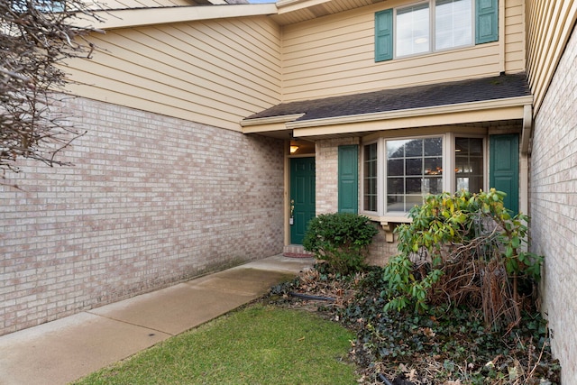 view of exterior entry with brick siding and a shingled roof