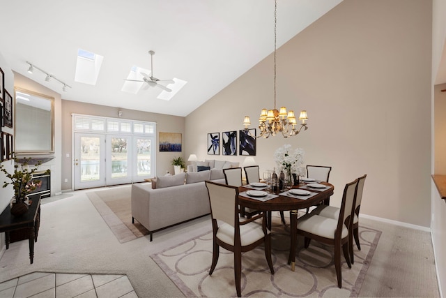 dining space featuring an inviting chandelier, rail lighting, light carpet, a skylight, and high vaulted ceiling