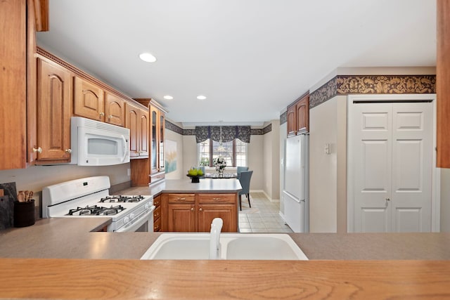 kitchen featuring light tile patterned floors, a sink, white appliances, a peninsula, and brown cabinetry