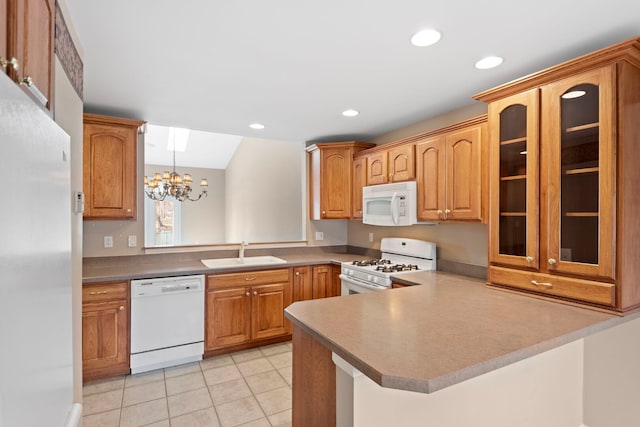 kitchen featuring glass insert cabinets, an inviting chandelier, a sink, white appliances, and a peninsula