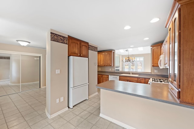 kitchen with light tile patterned floors, white appliances, a peninsula, a chandelier, and a sink