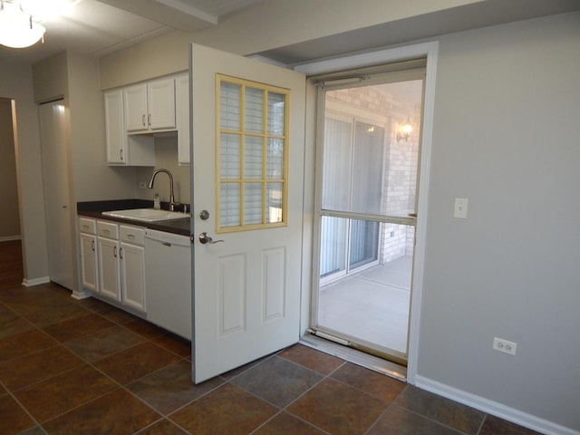 kitchen featuring white cabinets, dishwasher, baseboards, dark countertops, and a sink