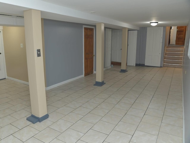 finished below grade area featuring light tile patterned flooring, baseboards, and stairway