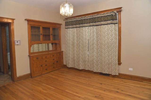 unfurnished dining area featuring baseboards, a notable chandelier, and wood finished floors