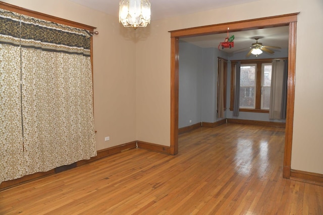empty room with baseboards, ceiling fan with notable chandelier, and hardwood / wood-style flooring