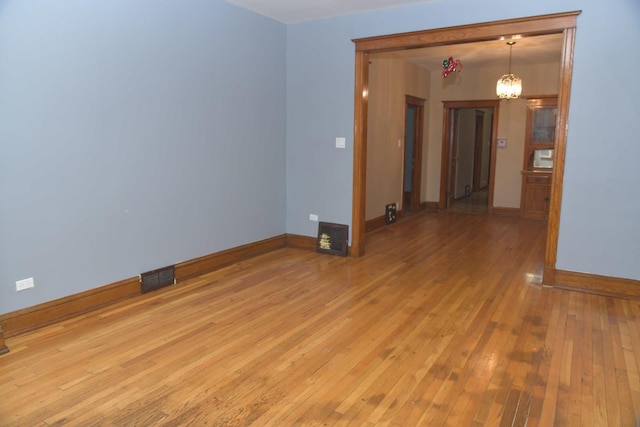 empty room with an inviting chandelier, baseboards, light wood-style floors, and visible vents