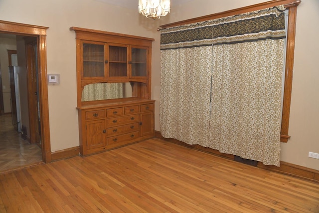 unfurnished dining area featuring baseboards, light wood-style floors, and a chandelier