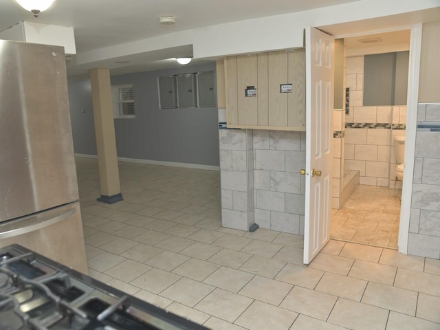 kitchen featuring freestanding refrigerator, light brown cabinetry, wainscoting, light tile patterned floors, and tile walls