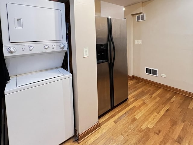 clothes washing area featuring light wood finished floors, baseboards, visible vents, and stacked washer / drying machine
