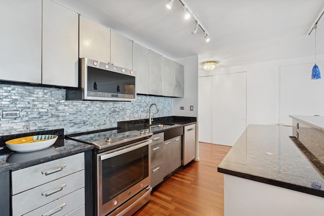 kitchen featuring stainless steel appliances, a sink, dark wood finished floors, tasteful backsplash, and hanging light fixtures