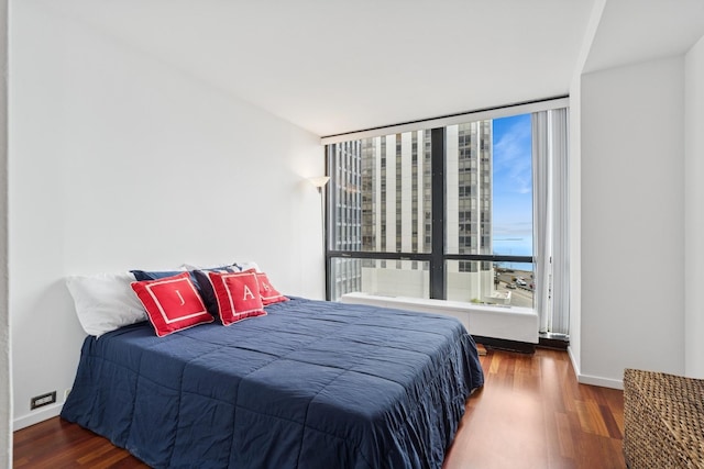 bedroom featuring baseboards, wood finished floors, and floor to ceiling windows