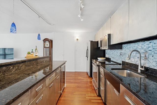 kitchen with stainless steel appliances, light wood-style flooring, a sink, decorative backsplash, and track lighting