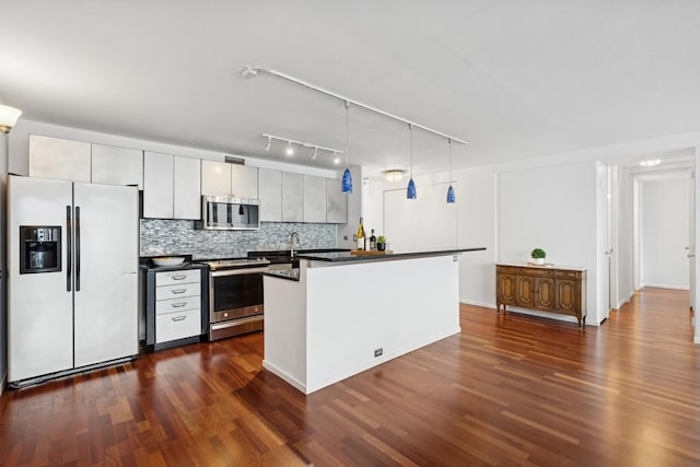 kitchen featuring stainless steel appliances, dark countertops, backsplash, pendant lighting, and dark wood-type flooring