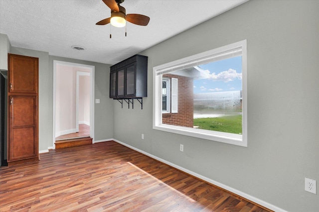 spare room with a textured ceiling, visible vents, baseboards, ceiling fan, and light wood-style floors