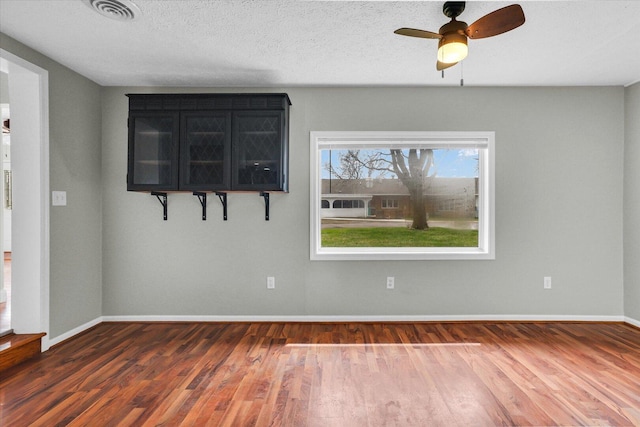 unfurnished room with a ceiling fan, wood finished floors, a textured ceiling, baseboards, and visible vents