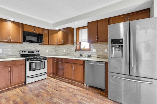 kitchen featuring light countertops, tasteful backsplash, stainless steel appliances, a sink, and light wood finished floors