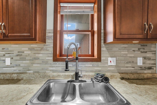 kitchen with backsplash, a sink, and light stone countertops