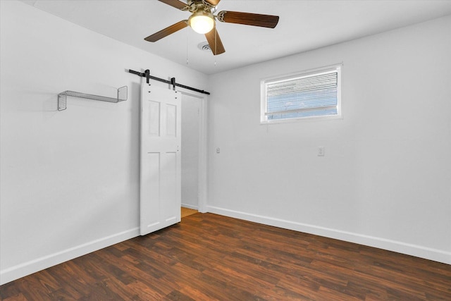unfurnished room with baseboards, a barn door, ceiling fan, and wood finished floors