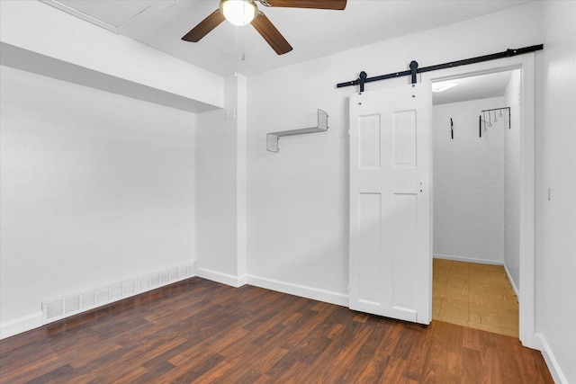 unfurnished room featuring visible vents, a barn door, wood finished floors, and a ceiling fan