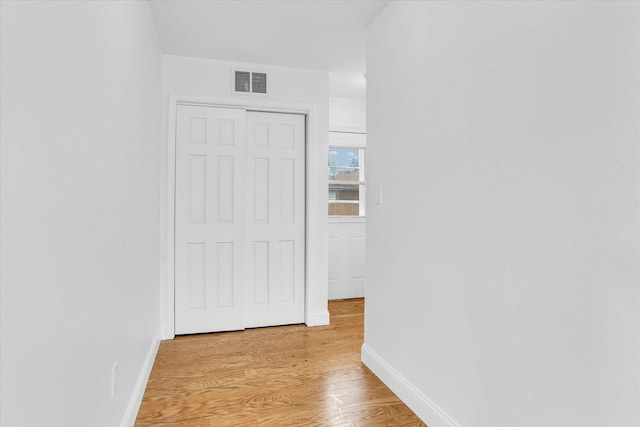 hall with light wood-style flooring, baseboards, and visible vents