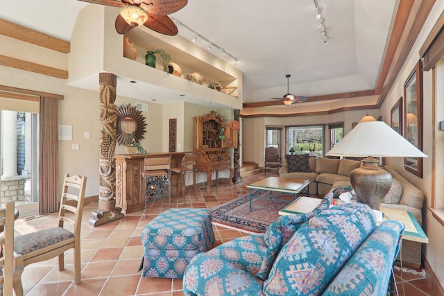 tiled living room with a warm lit fireplace, rail lighting, baseboards, ceiling fan, and a raised ceiling