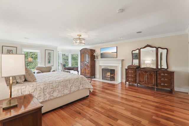 bedroom featuring light wood finished floors, a lit fireplace, ornamental molding, and a chandelier