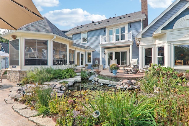 back of property featuring a balcony, a sunroom, roof with shingles, and a patio area