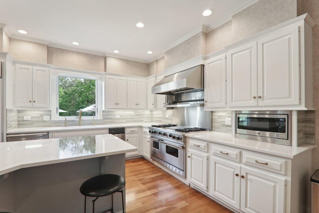 kitchen featuring crown molding, wall chimney exhaust hood, stainless steel appliances, white cabinetry, and a sink