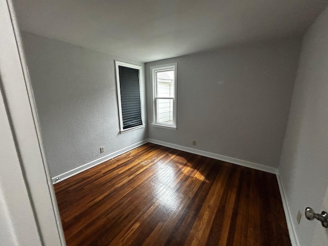 unfurnished room featuring dark wood finished floors, baseboards, and a textured wall