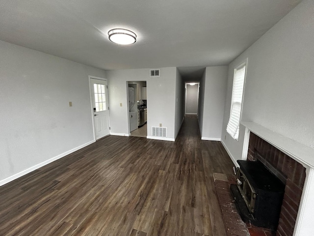 unfurnished living room with dark wood-style floors, visible vents, and a wood stove