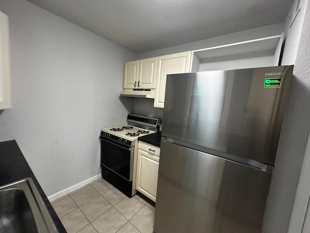 kitchen with freestanding refrigerator, under cabinet range hood, light tile patterned floors, baseboards, and range with gas cooktop