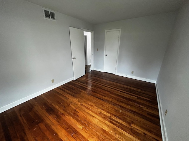 unfurnished room with baseboards, visible vents, and dark wood-type flooring