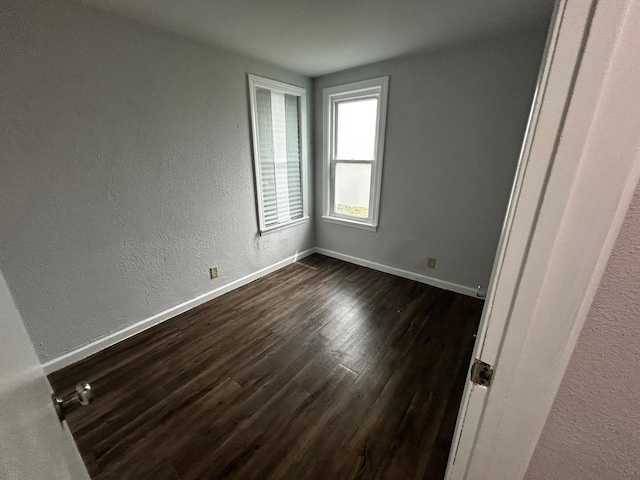 spare room featuring baseboards, a textured wall, and dark wood-style flooring