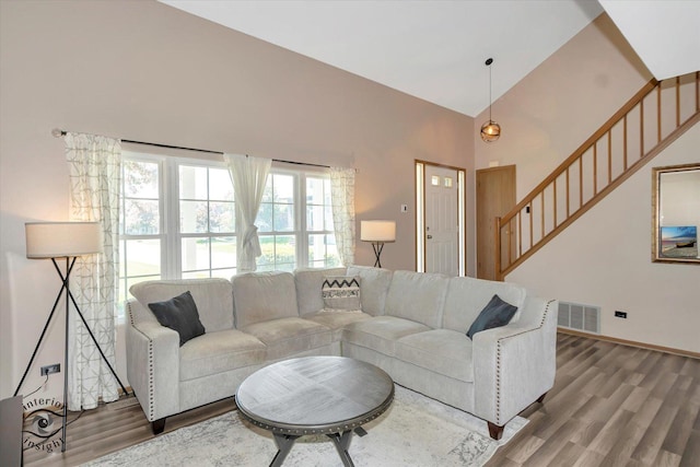 living room with wood finished floors, high vaulted ceiling, stairway, and baseboards