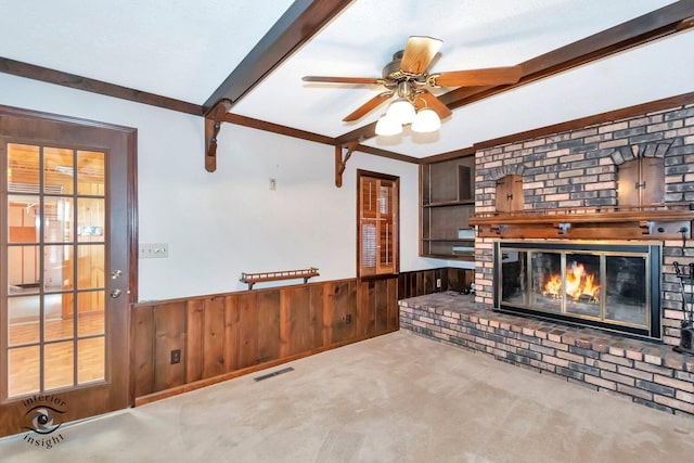 living room featuring a wainscoted wall, wooden walls, a brick fireplace, beamed ceiling, and carpet