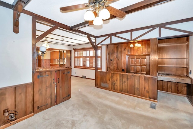 kitchen with light carpet, wood walls, wainscoting, brown cabinetry, and ceiling fan