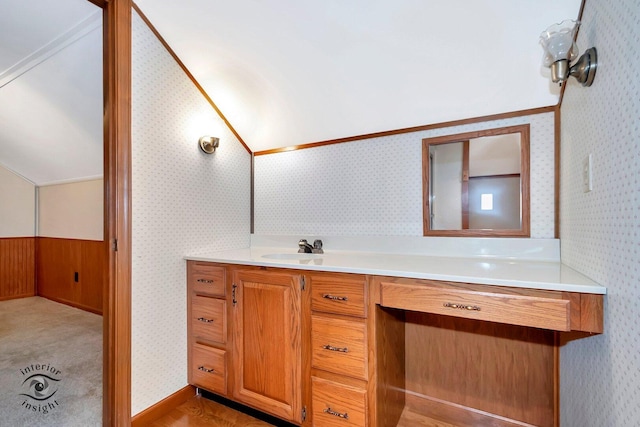 bathroom with vanity, lofted ceiling, wallpapered walls, and a wainscoted wall