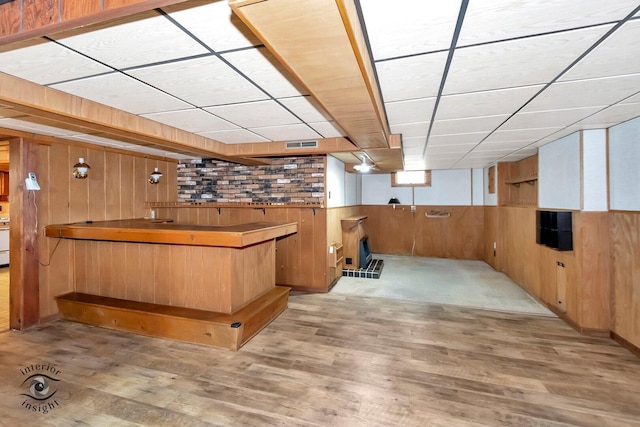 bar with a drop ceiling, wooden walls, bar, and wood finished floors